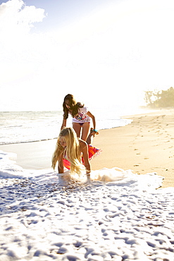 Two pre-teen girls play at Paia Beach, Maui, Hawaii and laugh as the wave gets them wet.