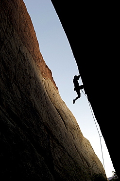 A rock climber is silhouetted as he ascends a red rock face in Nevada.