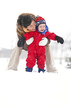 A two year old boy plays in a snowy field during a snowstorm in a red snowsuit with his mother in a park, Fort Collins, Colorado.