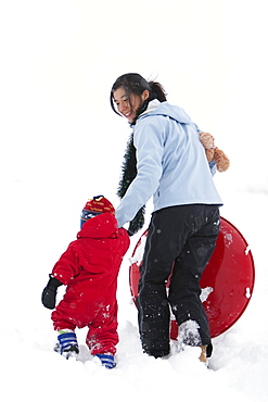 A two year old boy walks through the snow while holding his mother's hand during a day of sledding at the local sledding hill.