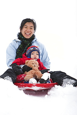 A two year old boy, sleds with his mother and his teddy bear at the local sledding hill in Fort Collins, Colorado.