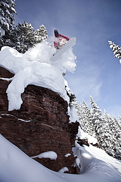 A snowboarder jumps off a cliff into powder in Colorado.