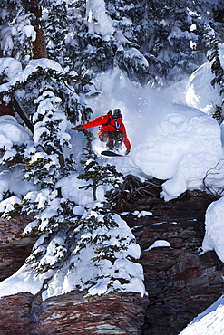 A snowboarder jumps off a cliff into powder in Colorado.