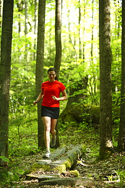 Woman trail running in a lush green forest.