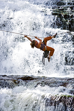 A woman crosses a waterfall using a Tyrolean Traverse on a rope.