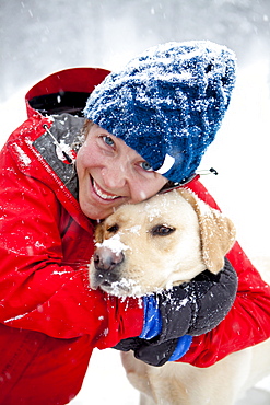 A woman gives her dog a loving hug on a snowy winter day.