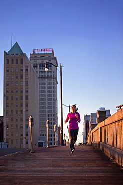 A teenage girl runs on a sidewalk at dusk in downtown Birmingham, Alabama with tall buildings in the background (hard lighting)