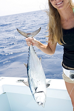 A mid adult blonde woman smiles as she holds up her freshly caught jack tuna.