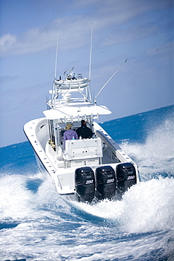 A fishing boat speeds through the blue surf spraying white water.