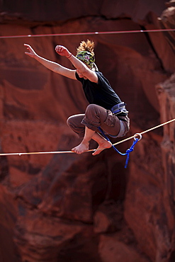 A female highliner stands up on a highline at the Fruit Bowl in Moab, Utah, USA.