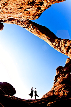 Couple doing tree posture yoga under the turret arch in Arches National Park.