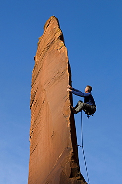 Man rock climbing up slender sandstone spire, Gateway, Colorado.