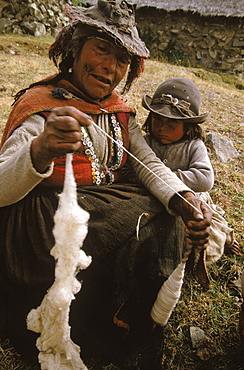 Elderly Quechua woman spins wool while her granddaughter looks on in Puma Chanca.