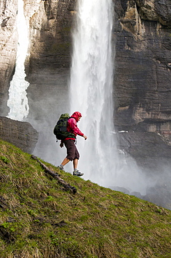 A woman hiking through water spray and spring ice below Bridal Veil Falls, Telluride, Colorado.