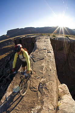 Mountain biker crossing sandstone bridge, Canyonlands, Utah.