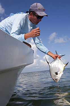 a fisherman holds up a freshly caught permit fish from the bow of his flats boat, San Pedro, Belize