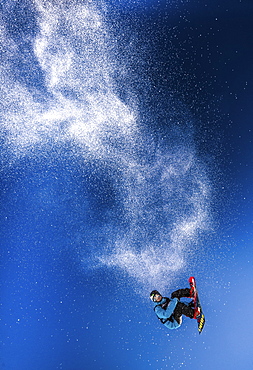 A snowboarder leaping into the air on the Dachstein-Glacier in Austria, leaving a trail of snow behind him.