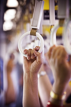 Hands holding hanging round handles in a subway car, Tokyo, Japan.