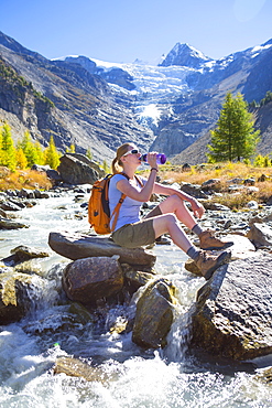 A female hiker relaxing near a river in the Swiss Alps. The region of Wallis, close to Zermatt. In the background is the Ried glacier. This valley is a paradise for outdoor enthusiasts like climbers, alpinists, hikers, mountainbikers and nature lovers. The water is directly coming from the glacier, so very refreshing after an excercise.