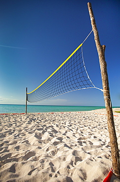 Two rough sticks hold up a beach volleyball net set up beside the ocean on Playa La Jaula beach, Cayo Coco, Cuba.