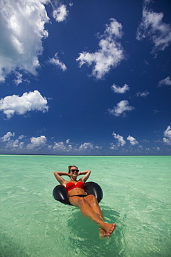 A young woman wearing a bikini relaxes on an inflatable tube in turquoise water while on vacation in Cayo Coco, Cuba.