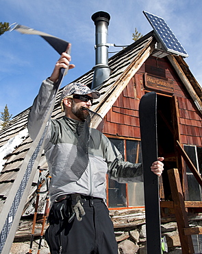 Skier putting climbing skins on skis in front of Peter Grubb Ski Hut, Sierra Nevada