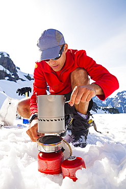 A climber uses a camping stove to make his dinner while camping in the mountains.