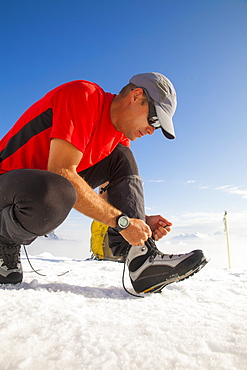 A climber ties up his mountaineering boot before heading toward the summit of Trio Peak in British Columbia, Canada.