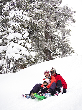 Parents and kids sledding in fresh snow in front of the Peter Grubb ski hut, Sierra Nevada