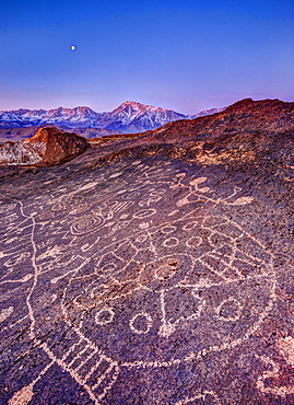 Piute Petroglyphs and full moon at sunrise with snow-capped Sierra in background, Eastern Sierra, California