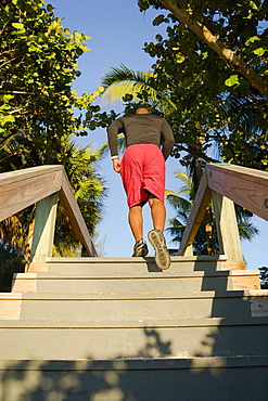 A man runs up stairs of an outdoor boardwalk in a tropical setting