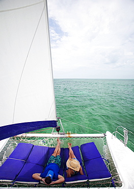 A couple lounge on the front of a catamaran enjoying a cruise in the Caribbean, Belize