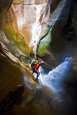 Man rappelling down canyon through waterfall in Utah.