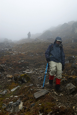 Surrounded by fog, two men descend a rocky slope in mountains of Butan.