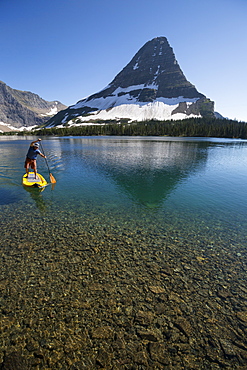 A man stand up paddle boards (SUP) on a calm Hidden Lake in Glacier National Park.