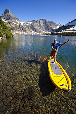 A man stand up paddle boards (SUP) on a calm Hidden Lake in Glacier National Park.