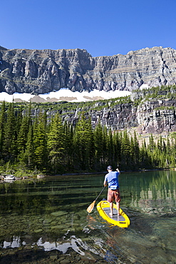 A man stand up paddle boards (SUP) on a calm Hidden Lake in Glacier National Park.