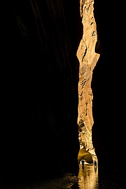 Two silhouetted figures hiking in a narrow slot canyon in the desert.