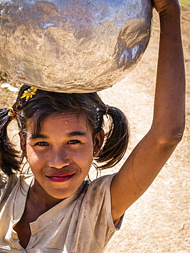 Young woman carrying water in an aluminum jug on her head.