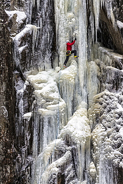 A man in a red jacket is climbing on ice.