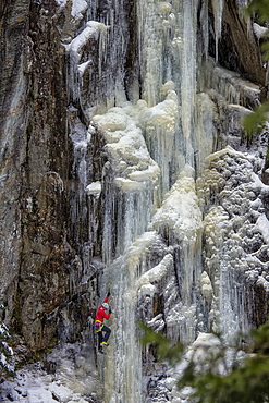 A man in a red jacket is climbing on ice.