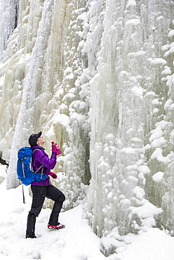 A woman hiker looking up at a tall wall of ice and snow.