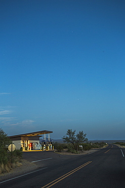 A Vintage Gas Station Glows Beside An Empty Desert Road At Dawn