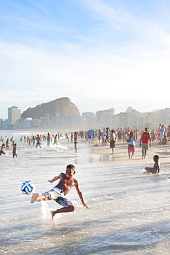 A Little Boy Kicks A Soccer Ball In The Surf Of Copacabana Beach, Rio De Janeiro, Brazil