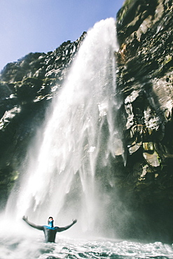 A Man In A Wetsuit Stands Under A Big Waterfall In The Faroe Islands