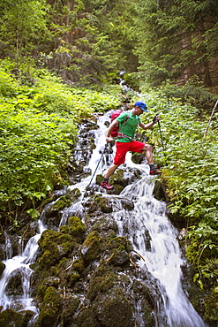 Male hiker stepping over mountain river stream in woods