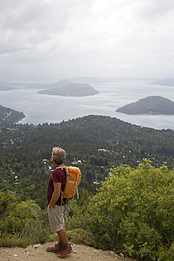 Mature hiker pauses on trail above lakes and mountains