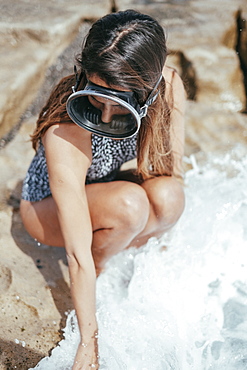 girl in a swimsuit and diving googles playing with the waves on the beach