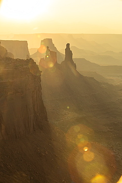 An orange sun beam cuts through rock formations in Canyonlands National Park in Moab Utah at sunrise.