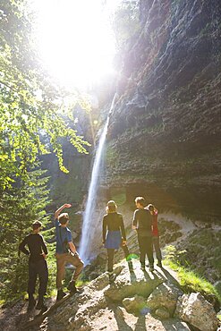 Group of young people standing at foot of Pericnik waterfall in alpine Vrata valley near Mojstrana in Triglav National Park, Slovenia